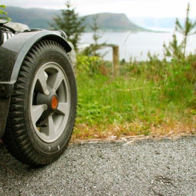 Bilde av hjulet til et assistansekjøretøy som står parkert på gress med utsikt over sjøen.