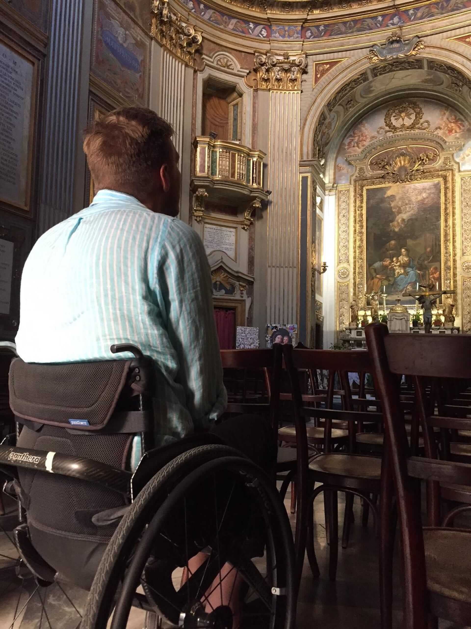 Bilde av artikkelskribent i rullestol inne i en kirke. Han sitter med ryggen mot kameraet og kikker mot et alter. Han er alene.
