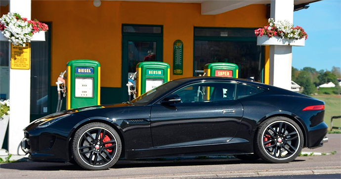 Bilde av en svart sportsbil. Den står parkert foran en landlig bensinstasjon med gammeldagse pumper. I bakgrunnen skimtes en søyle til høye og en til venstre, begge med blomsterkasser