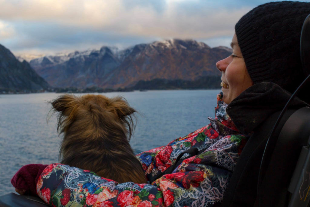 Nærbilde av artikkelskribent som sitter ute. Hun har en hund på fanget og de kikker begge ut mot fjorden. I bakgrunnen skimtes vann og fjellformasjoner.