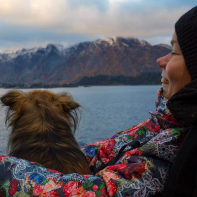 Nærbilde av artikkelskribent som sitter ute. Hun har en hund på fanget og de kikker begge ut mot fjorden. I bakgrunnen skimtes vann og fjellformasjoner.