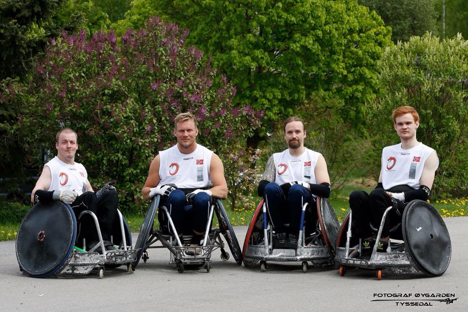 Bilde av Lars Ivar Eilerås sammen med tre lagkamerater i rullestolrugby. De sitter alle i rullestol ved siden av hverandre i hvite trøyer. I bakgrunnen skimtes trær.