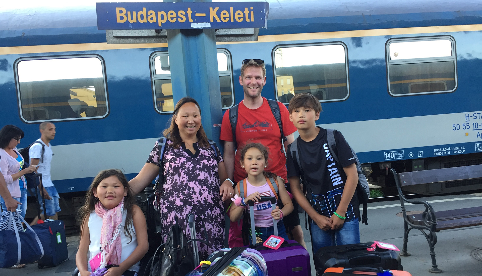Bilde av BPA-koordinator Elisabeth Lillegrend sammen med sin ektemann, sønn og to døtre. De står samlet på en perrong med bagasje foran seg. I bakgrunnen skimtes et tog og et skilt med påskriften «Budapest – Keleti».