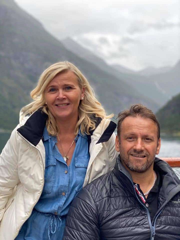 Shaqir og Vigdis på ferje i fjorden. Fjell i bakgrunnen. De smiler mot kamera.