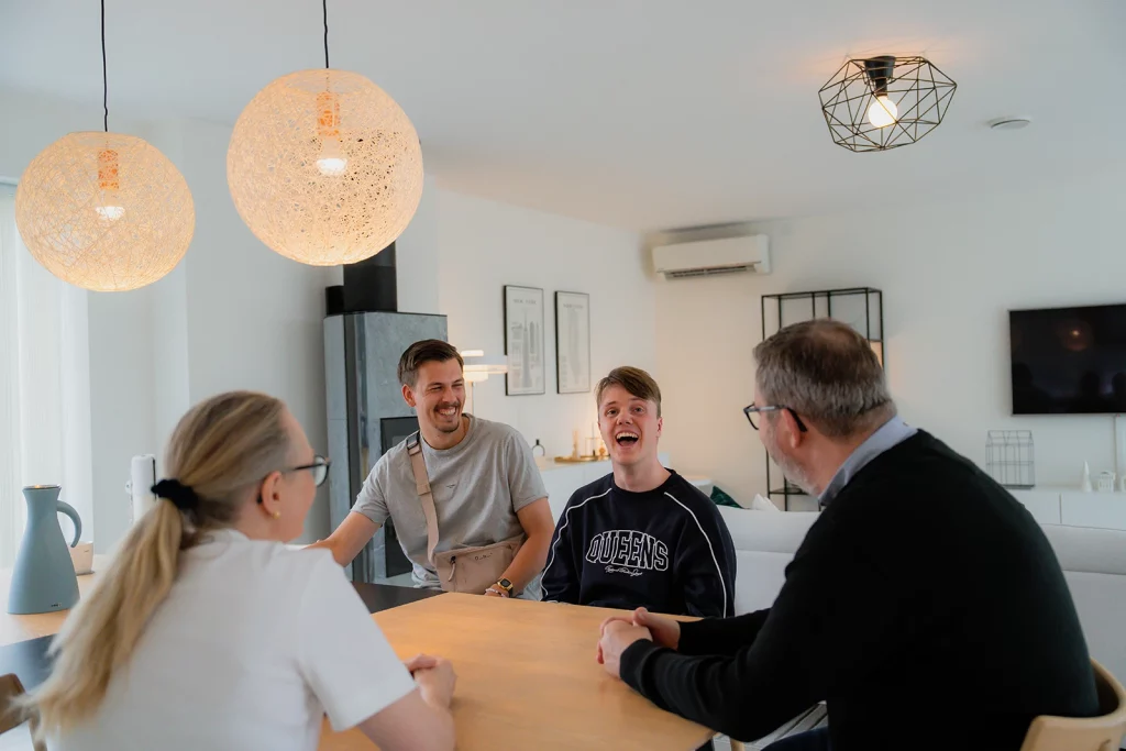 Familie på 3, sammen med assistent. Alle smiler og ler rundt spisebordet.