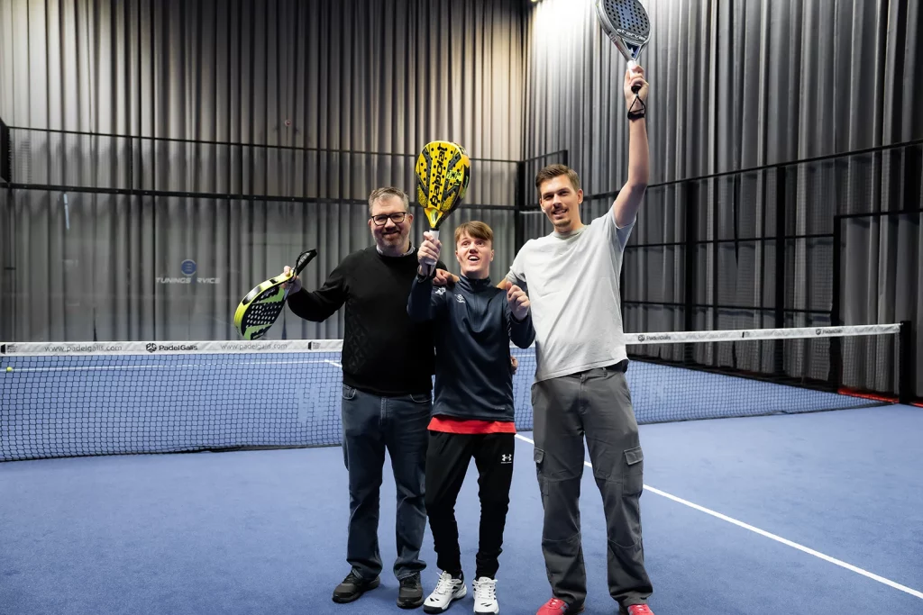 far, sønn og mannlig assistent som vifter med Padel racket. Alle smiler etter en god Padel kamp.