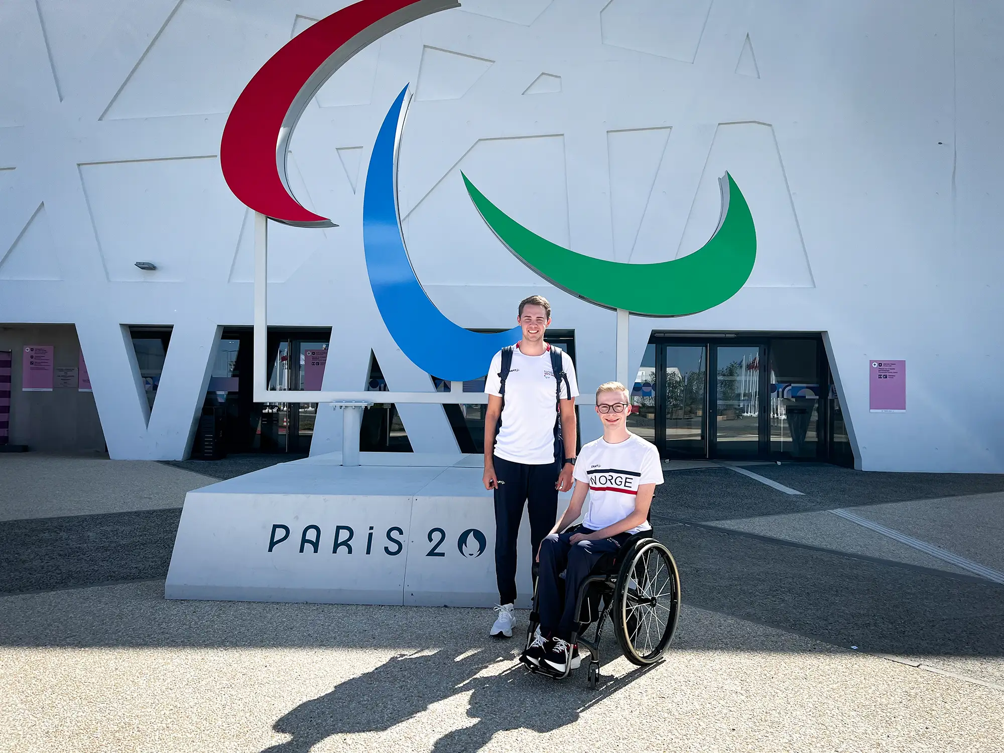 Martin og BPA-assistent foran Paralympics Paris 2024-skilt. Begge smiler.