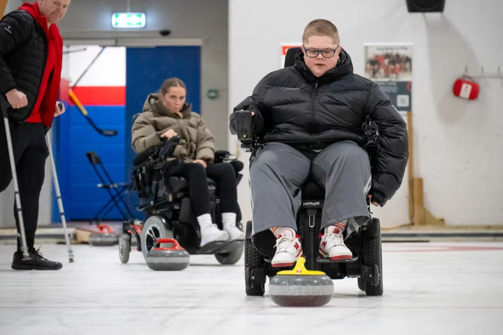 gutt i rullestol som spiller curling på isbane