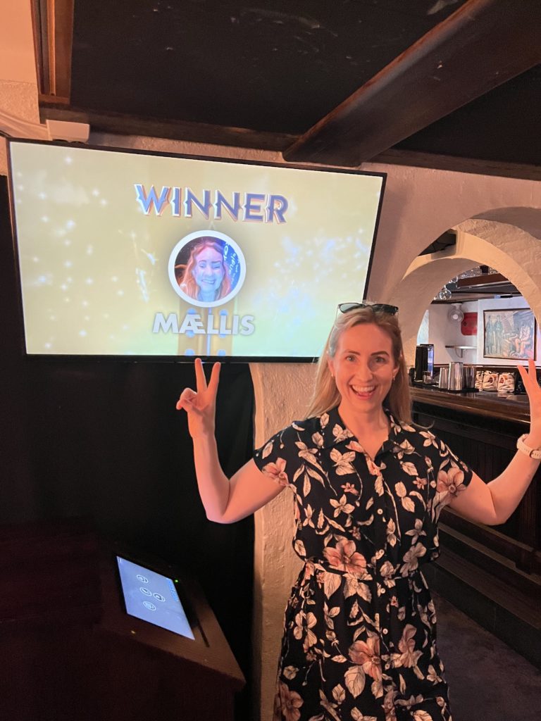 dame som står og smiler foran skjerm. på skjermen står det "winner"