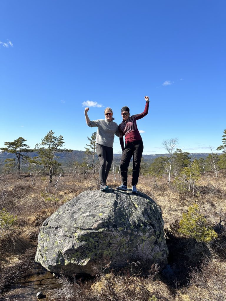 to damer med armene i været som står på en stor stein