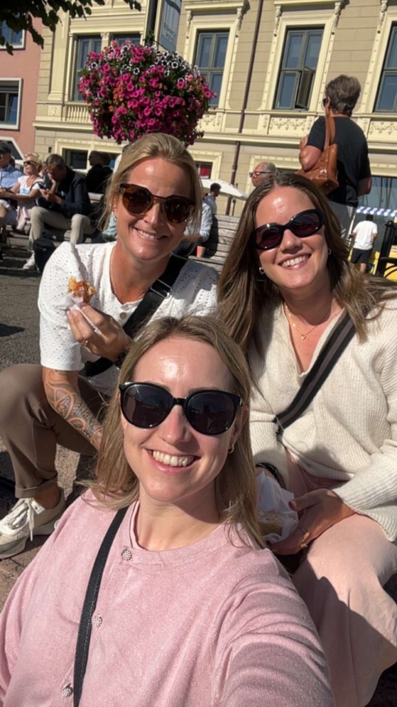 tre damer med solbriller som smiler mot kamera