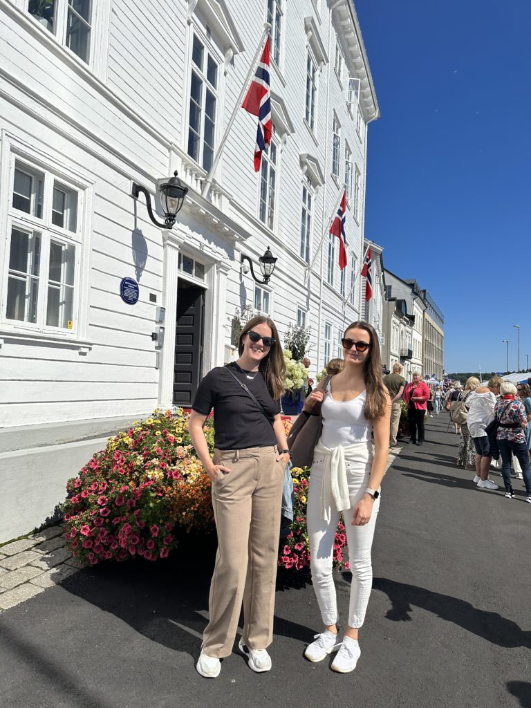 to damer som står oppstilt foran hvitt bygg