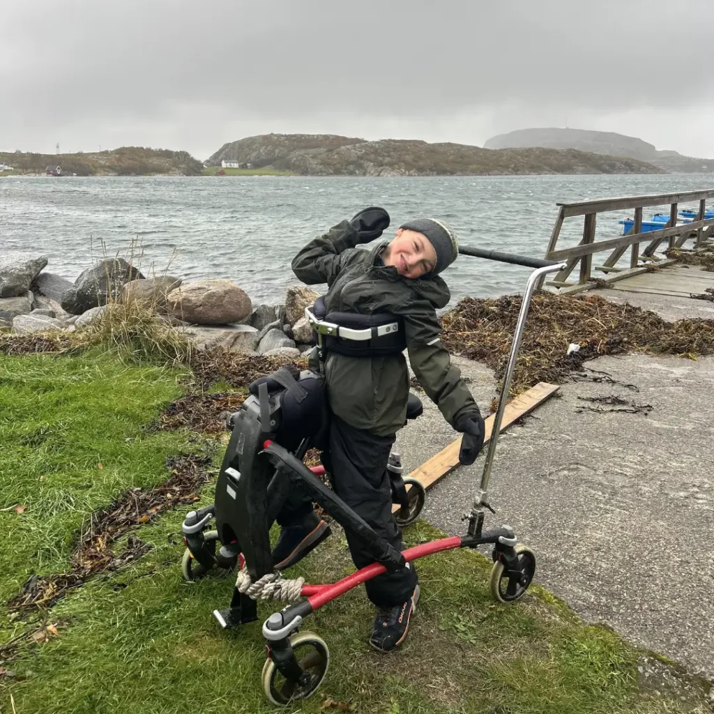 Ung gutt i frame running stol som smiler mot kamera. bildet er tatt langs kysten med havet som bakgrunn